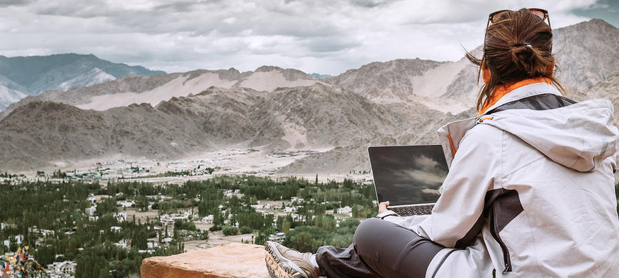 Traveler with laptop sits on top view point on the mountain valley