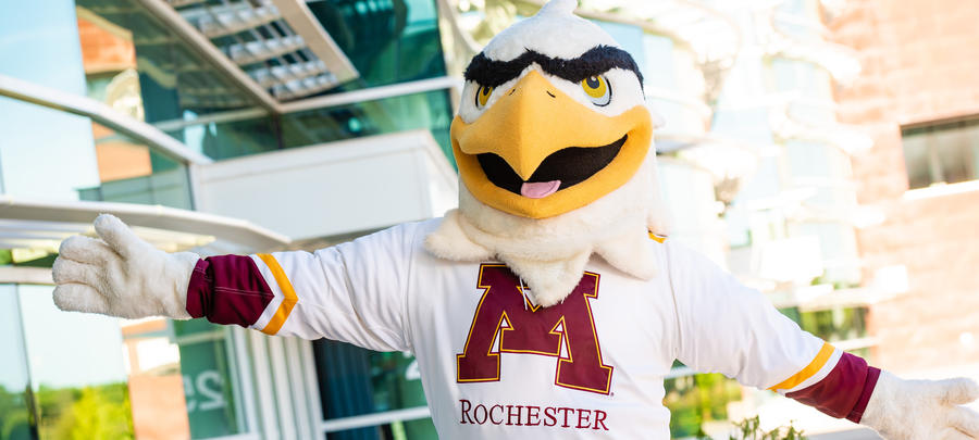 Rockie the Raptor mascot standing in front of building on a sunny day. 