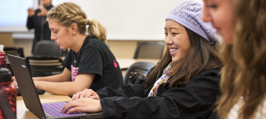 A University of Minnesota Rochester student smiles while working on her laptop in a classroom with students.