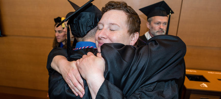 Faculty and student hugging in cap and gowns at commencement. 