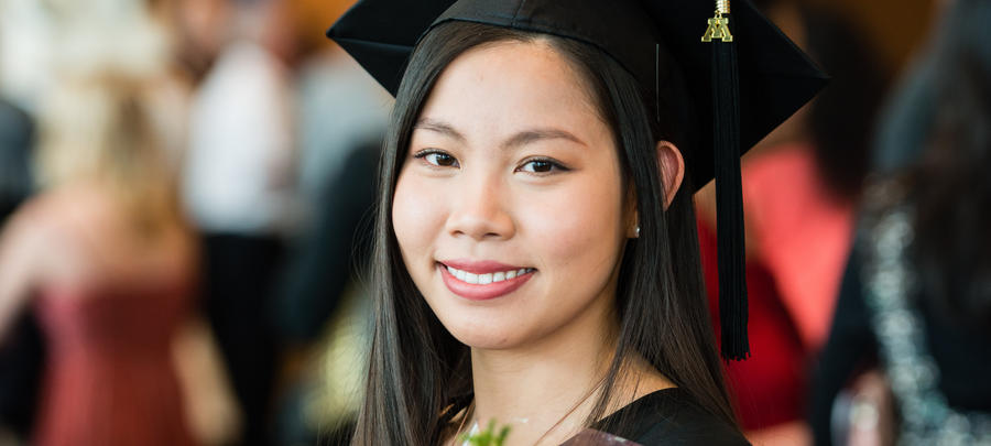 Female graduate smiling with pink flowers and diploma in hand. 