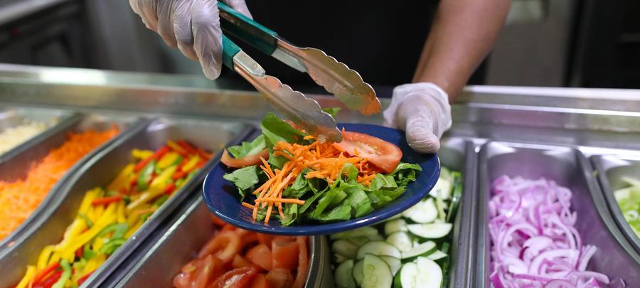 Closeup photo of a salad bar and worker serving a plate of food. 